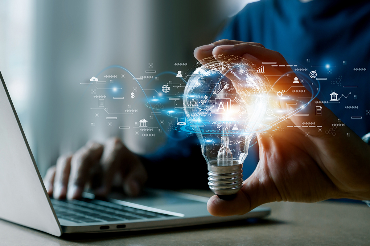 Person holding an illuminated light bulb with an AI graphic near a laptop