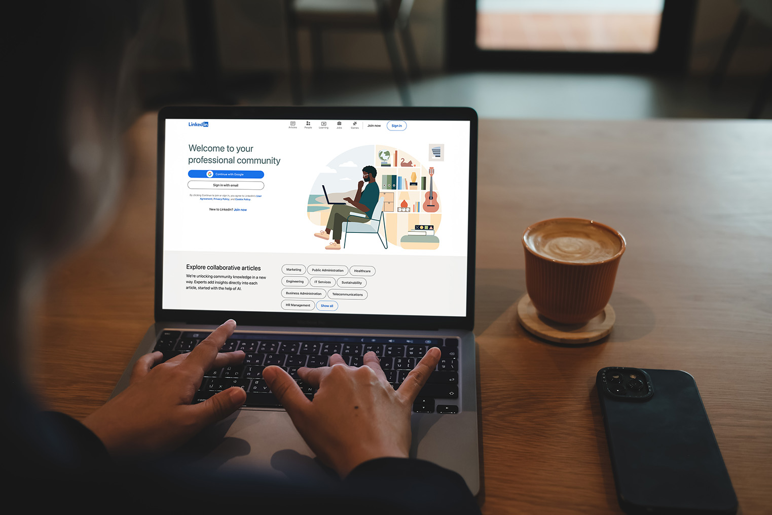 Person using LinkedIn on a laptop beside a coffee and phone
