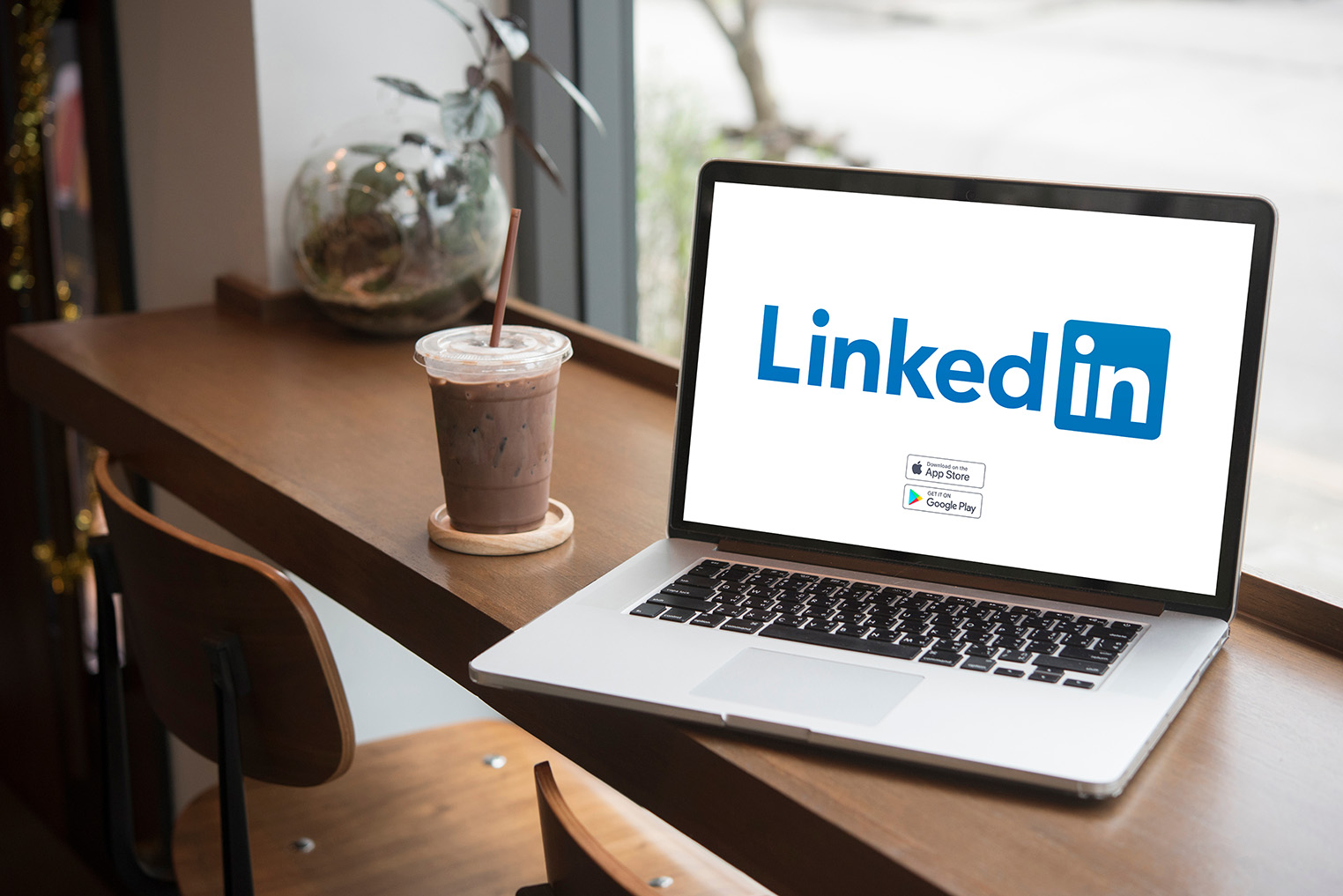 Laptop displaying the LinkedIn logo beside an iced drink