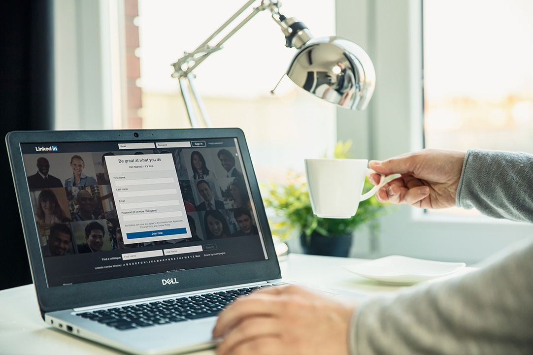 Person using LinkedIn on a laptop while holding a coffee cup