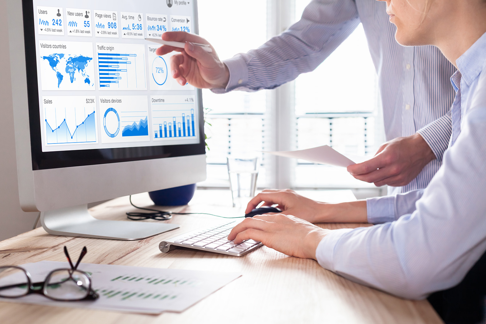 Two colleagues reviewing charts on a desktop monitor